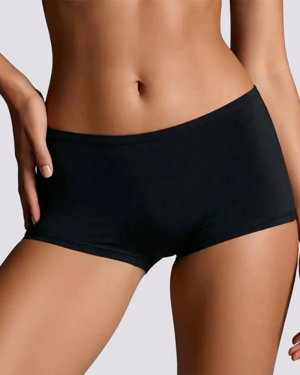 A close-up of a model wearing black high-waisted briefs against a light gray studio background.