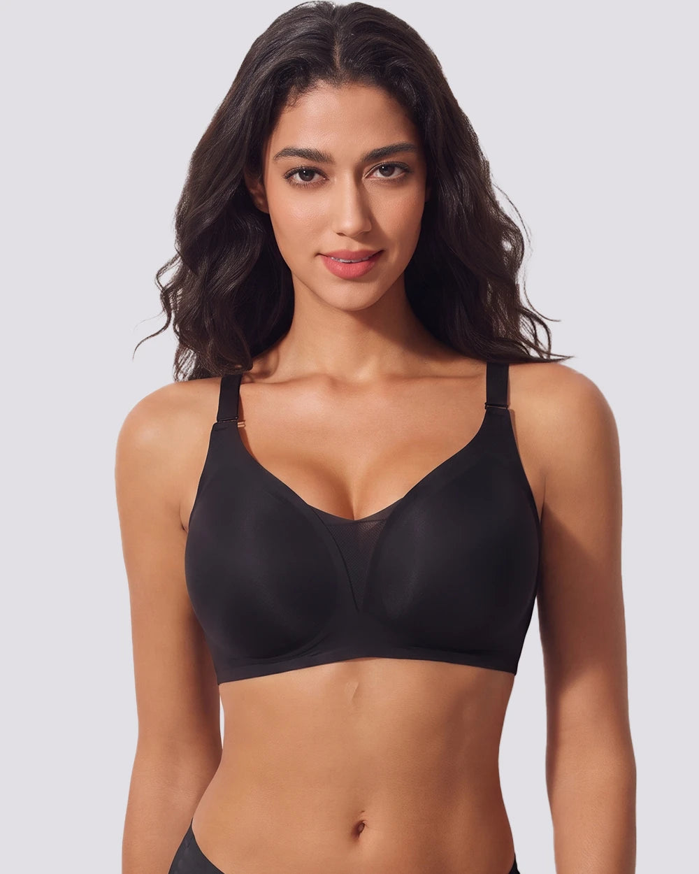 A woman modeling a black wireless bra with wide adjustable shoulder straps against a light gray studio background.