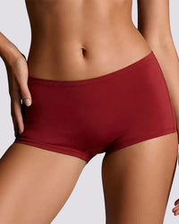 A close-up of a model wearing solid dark red high-waisted briefs against a light gray studio background.