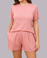 A woman wearing a matching two-piece loungewear set in a dusty pink color, featuring a short-sleeve crewneck t-shirt and matching drawstring shorts, shown against a solid gray background.