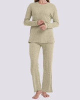A woman modeling a two-piece ribbed knit pajama set in a light sage green color, consisting of a long-sleeve top and matching pants, against a solid light gray background.