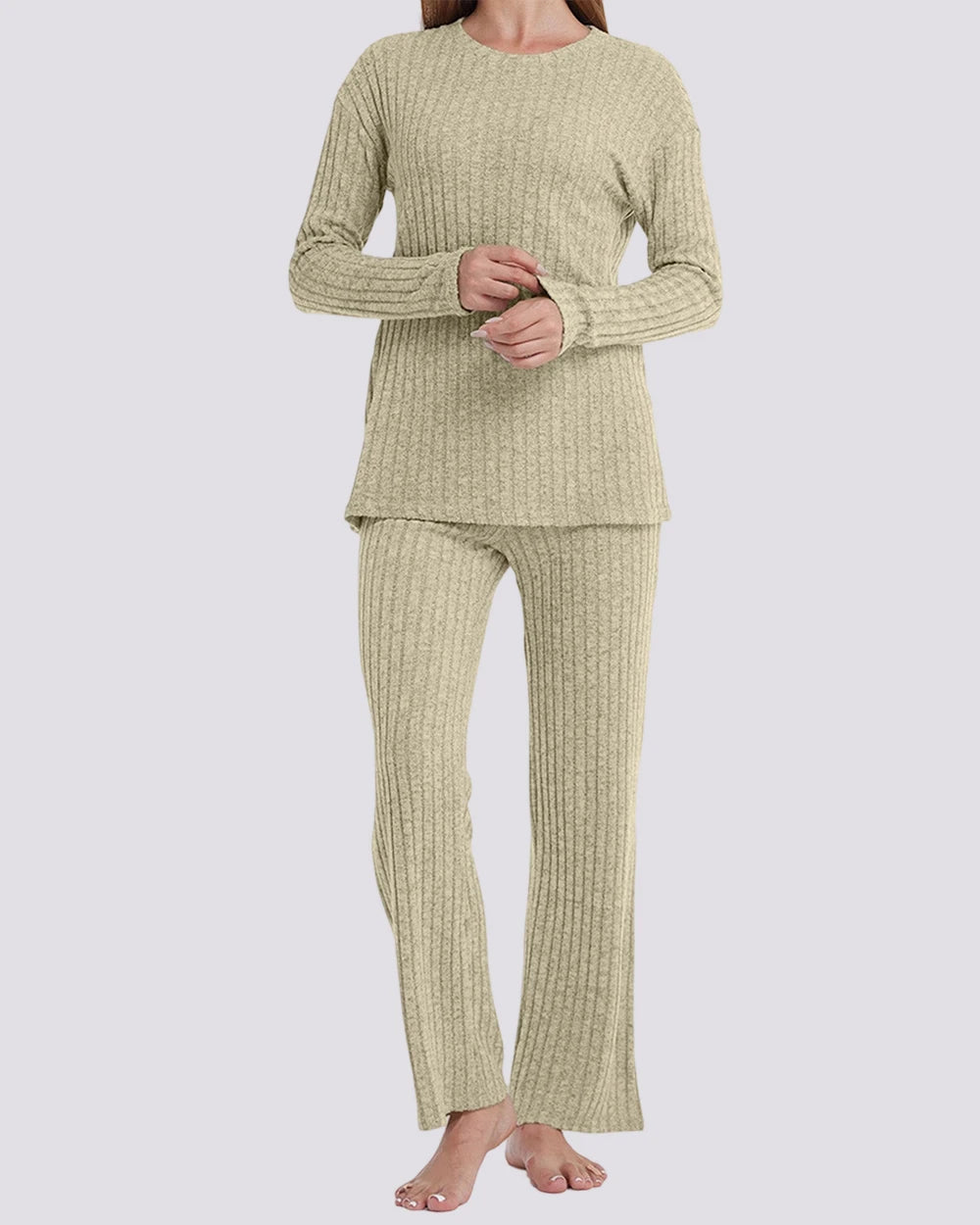A woman modeling a two-piece ribbed knit pajama set in a light sage green color, consisting of a long-sleeve top and matching pants, against a solid light gray background.