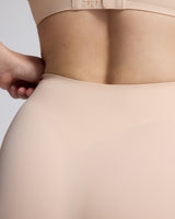 Close-up of a model wearing a seamless high-waisted shapewear brief in a light nude beige color, showing the waistband and hip area.