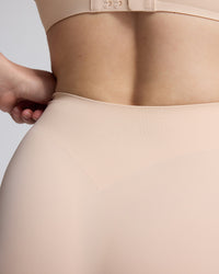 Close-up of a model wearing a seamless high-waisted shapewear brief in a light nude beige color, showing the waistband and hip area.