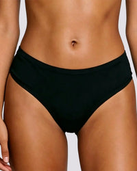A close-up of a model's midsection wearing black bikini bottoms against a light gray background.