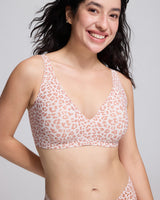 A smiling woman wearing a pink leopard print wireless bra with a seamless bralette design, photographed against a clean light gray studio background.