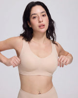 A woman modeling a light beige wireless bra and matching underwear against a plain light gray studio background.