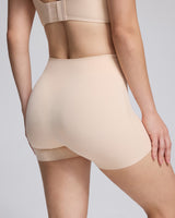 Close-up back view of a model wearing high-waisted seamless shapewear shorts in a light nude beige color, paired with a matching bralette.