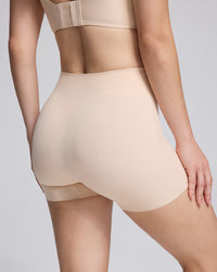 Close-up back view of a model wearing high-waisted seamless shapewear shorts in a light nude beige color, paired with a matching bralette.