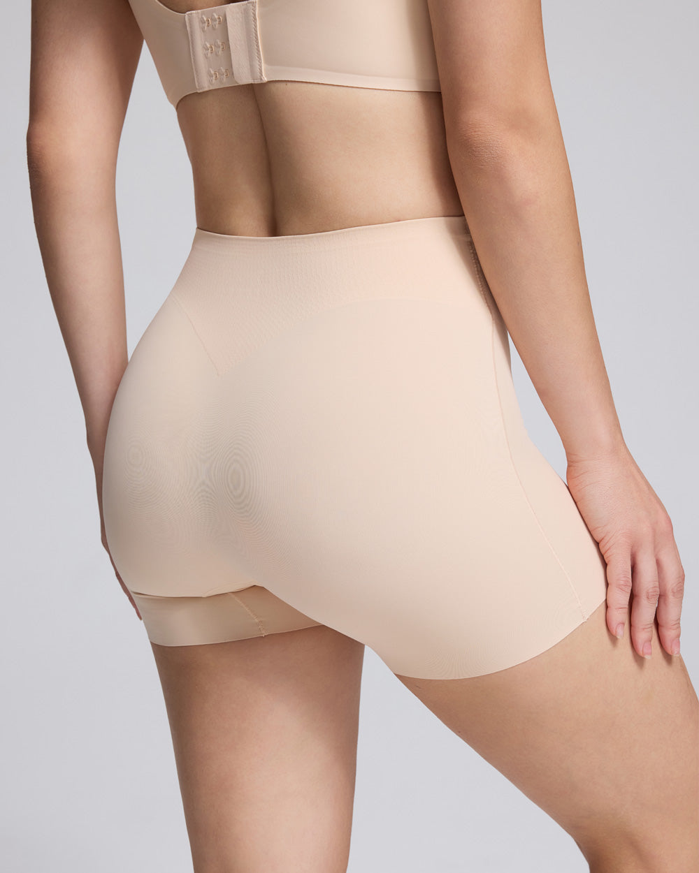 Close-up back view of a model wearing high-waisted seamless shapewear shorts in a light nude beige color, paired with a matching bralette.