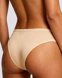 Rear view of a model wearing high-waisted, seamless beige underwear against a light gray background.