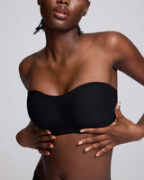 A close-up of a model wearing a black strapless bandeau tube top against a light gray studio background.