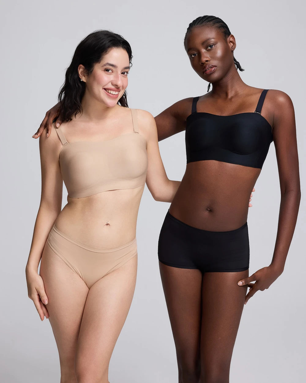 Two models wearing seamless underwear sets in nude beige and black, standing against a light gray studio background.
