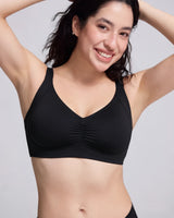 A woman wearing a black wireless bralette with a V-neckline and gathered center detail, posing against a light gray studio background.