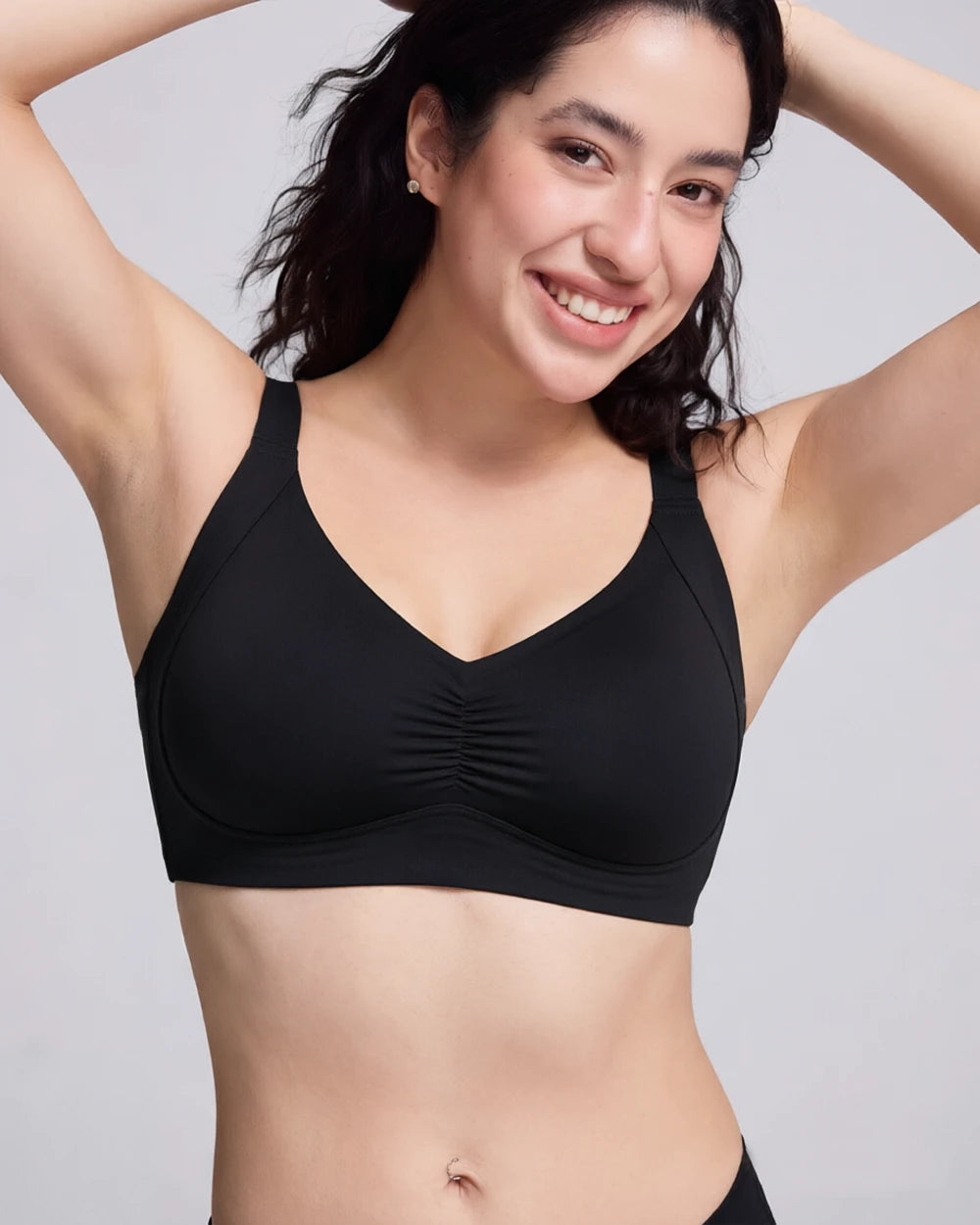 A woman wearing a black wireless bralette with a V-neckline and gathered center detail, posing against a light gray studio background.