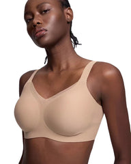 A woman wearing a seamless, molded-shape bra in a light beige shade, shown from the chest up against a plain white background.