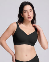 A woman modeling a  VRCOMFY black wireless bra with a V-neckline against a solid light gray background.