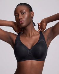 A model wearing a vrcomfy black wireless bra with seamless cups, posing against a solid light gray background.