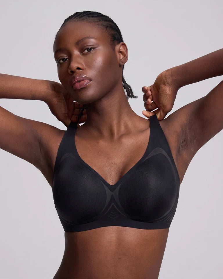 A model wearing a vrcomfy black wireless bra with seamless cups, posing against a solid light gray background.