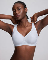 A woman modeling a vrcomfy blue wireless bra against a light gray studio background.