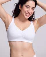 A smiling woman wearing a white wireless bralette with a V-neckline and subtle gathered detailing at the center bust, photographed against a light gray studio background.
