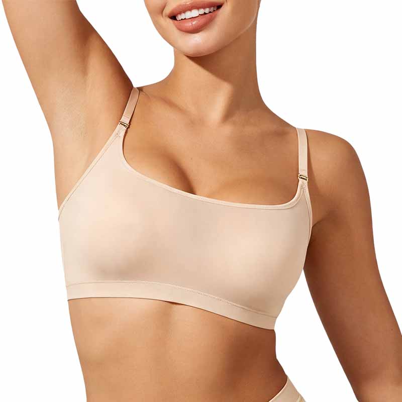 A close-up of a woman wearing a light beige seamless bralette with thin adjustable straps against a plain white background.