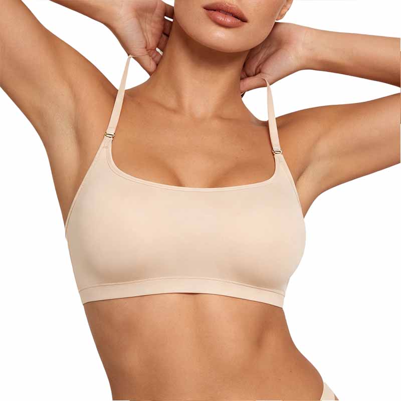 A close-up of a model wearing a beige seamless bra with thin adjustable straps and small silver metal adjusters, set against a plain white background.