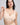 A woman modeling a light beige wireless bra against a solid light gray background.