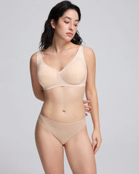 A woman modeling a matching vrcomfy beige/nude bra and underwear set against a plain light gray studio background.