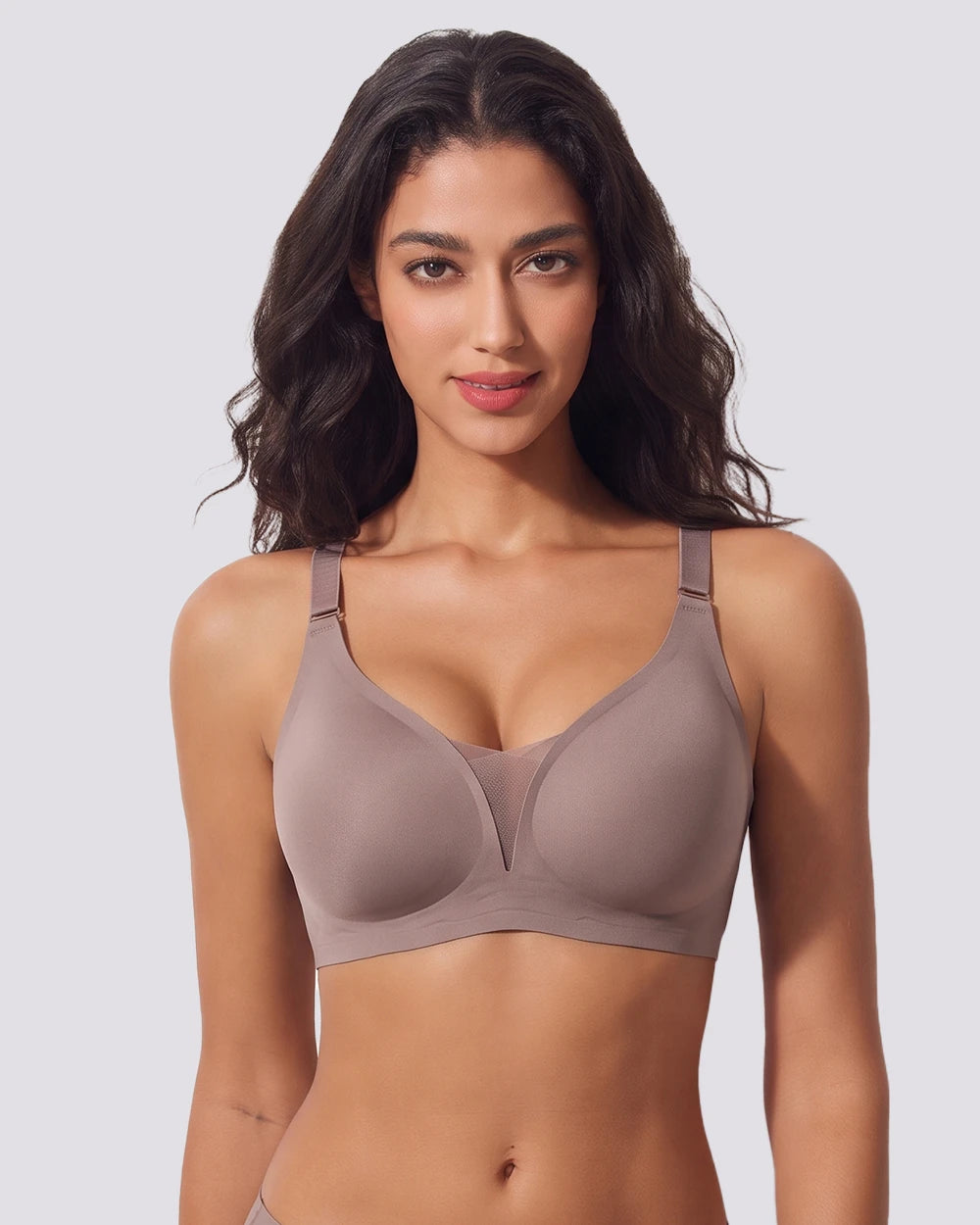 A woman modeling a seamless, wireless bra in a muted taupe-brown color, shown from the waist up against a solid light gray background.