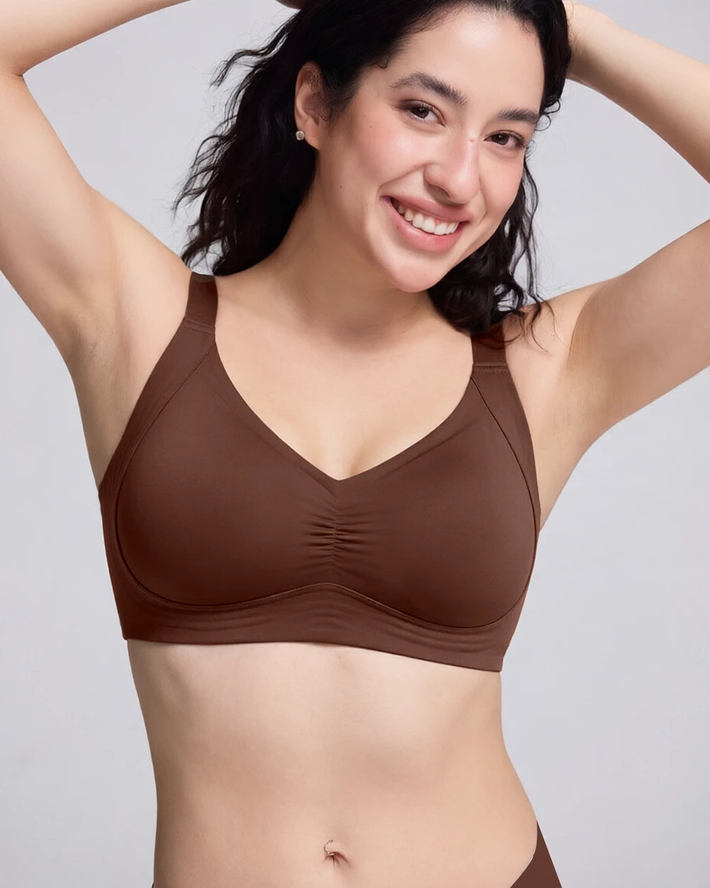 A woman wearing a brown V-neck bralette with a gathered center front, shown against a light gray studio background.