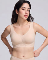 A woman modeling a light beige wireless bra with a gathered center front, shown against a plain light gray studio background.