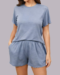 A woman wearing a light blue two-piece loungewear set consisting of a short-sleeve crewneck t-shirt and matching drawstring shorts, shown against a solid gray studio background.