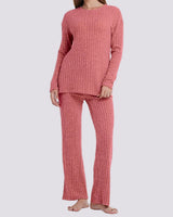 A woman modeling a two-piece ribbed knit loungewear set in a dusty rose pink color, consisting of a long-sleeve top and matching pants, against a solid light gray background.