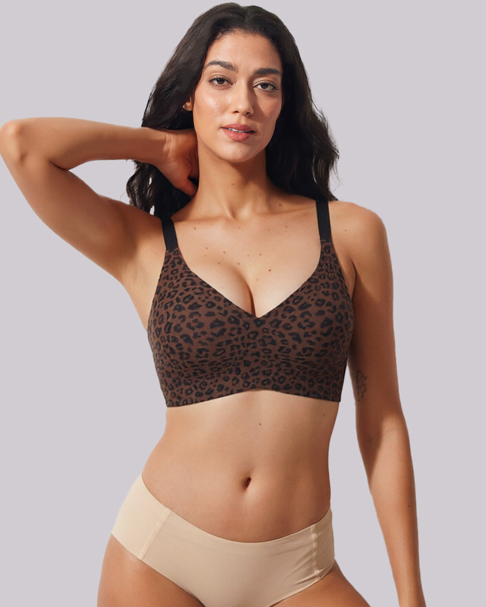 A woman modeling a leopard-print underwire bra and beige high-waisted briefs against a solid light gray background.