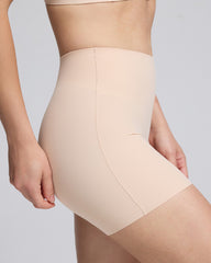 Close-up of a model wearing high-waisted shapewear shorts in a light nude beige color, showing the waistband, center seam, and hip contour against a plain light gray background.