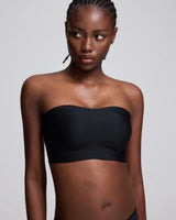 A woman modeling a black strapless bandeau-style bra top against a light gray studio background.