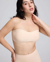 A woman modeling a strapless bandeau-style bra in a light nude beige color, paired with matching high-waisted shorts, against a solid light gray studio background.