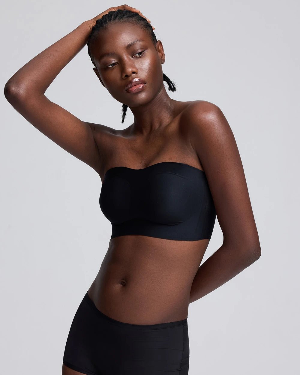 A model wearing a black strapless bandeau tube top and matching black bottoms, posing against a solid light gray background.