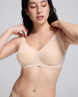 A woman wearing a nude-beige seamless underwire bra with textured foam cups, posing against a light gray studio background.
