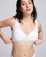 A woman modeling a vrcomfy white seamless underwire bra with molded cups, shown from the chest down against a light gray studio background.