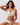 A woman modeling a matching beige wireless bra and high-waisted brief set against a light gray studio background.