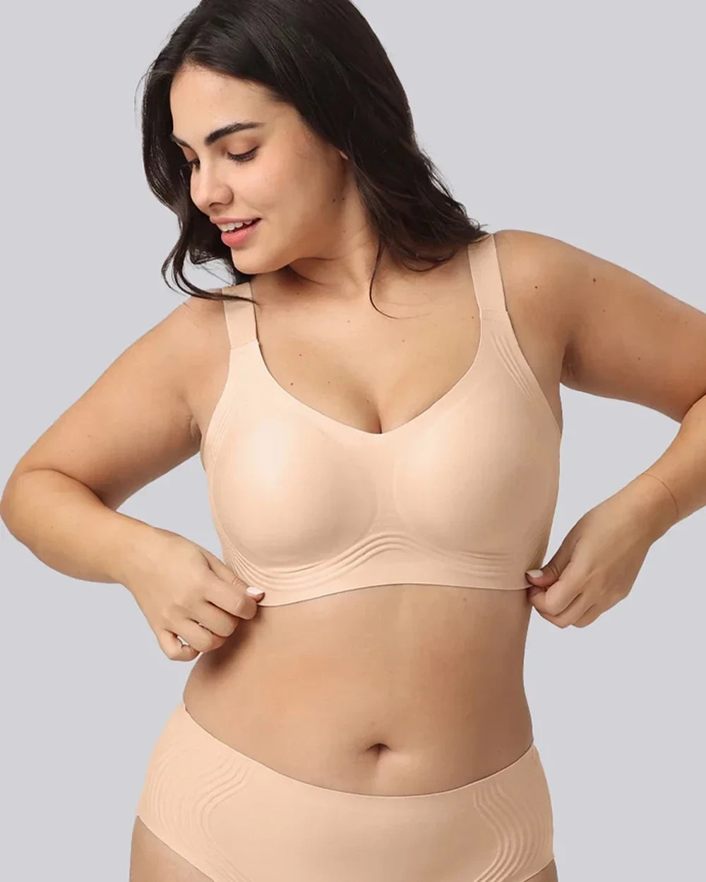 A woman modeling a light beige wireless bra and matching underwear against a solid gray background.